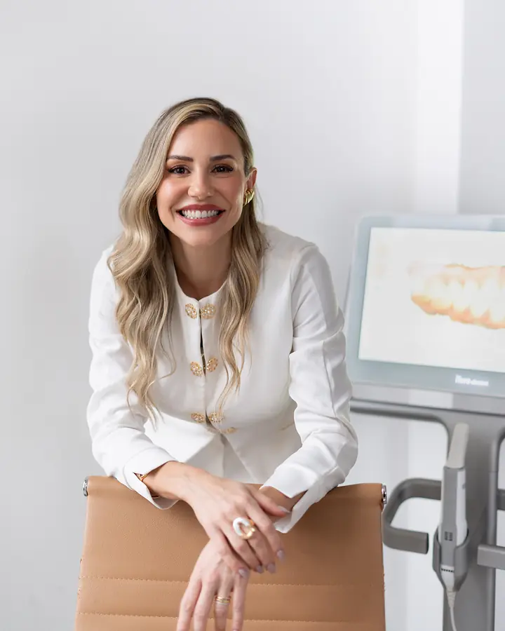 Dra. Alice Freitas sorrindo no consultório, ao lado do scanner digital 3D usado na avaliação de Invisalign