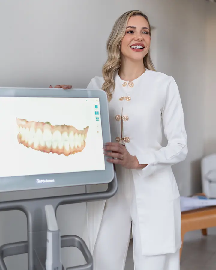 Dra. Alice Freitas ao lado da tela do scanner iTero, que mostra o escaneamento 3D de uma arcada dentária