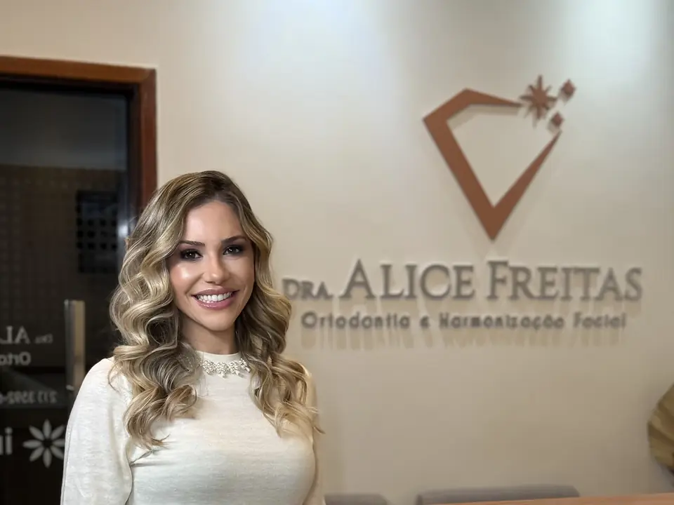 Dra. Alice Freitas na recepção da clínica, com o logotipo na parede, no Alfa Barra I, Barra da Tijuca
